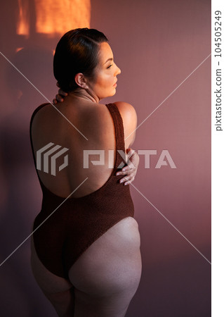 Back view of body positive black lady posing, hugging her bare shoulder Back view of body positive black lady posing, hugging her bare shoulder 104505249