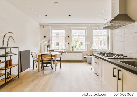 a kitchen and dining area in a small apartment with white walls, wood flooring and marble countertops on either side a kitchen and dining area in a small apartment with white walls, wood flooring and marble countertops on either side 104505808