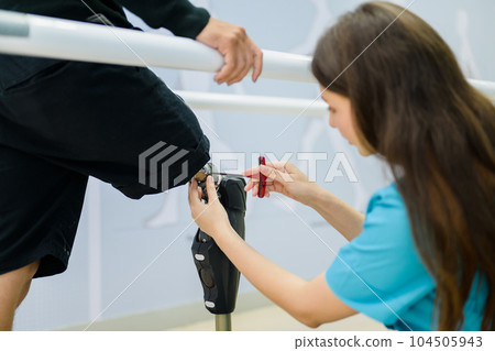 Female physiotherapist adjusting prosthetic leg of patient in hospital 104505943