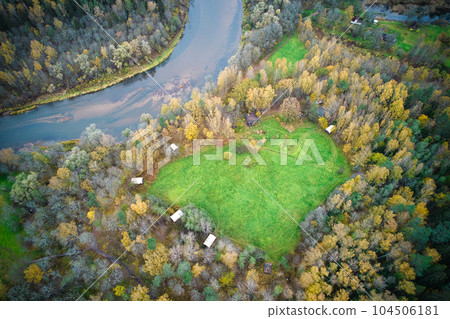 This photo features a heart-shaped lawn in the middle of an autumn forest, located near a river. The image was captured on a cloudy day, adding a moody and atmospheric feel to the scene. 104506181