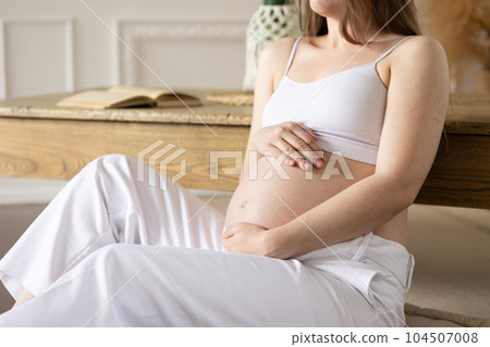 A pregnant girl sits on the floor leaning table Close-up of the abdomen concept calm happy pregnancy future motherhood A pregnant girl sits on the floor leaning table Close-up of the abdomen concept calm happy pregnancy future motherhood 104507008