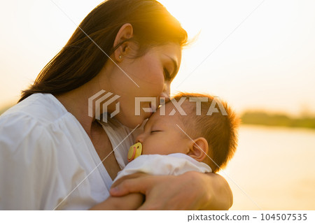 Loving mother holding and carrying her newborn baby with sunset view Loving mother holding and carrying her newborn baby with sunset view 104507535