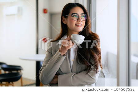 Smiling portrait of beautiful businesswoman with cup of coffee in office Smiling portrait of beautiful businesswoman with cup of coffee in office 104507552