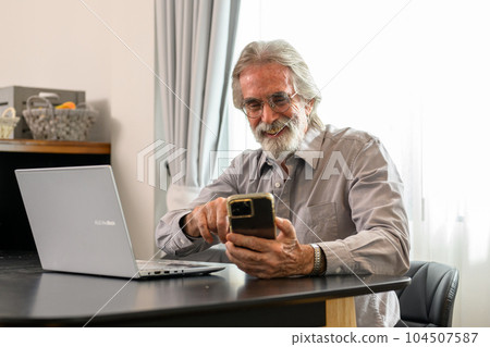 Senior grandfather using laptop and smart phone at home Senior grandfather using laptop and smart phone at home 104507587