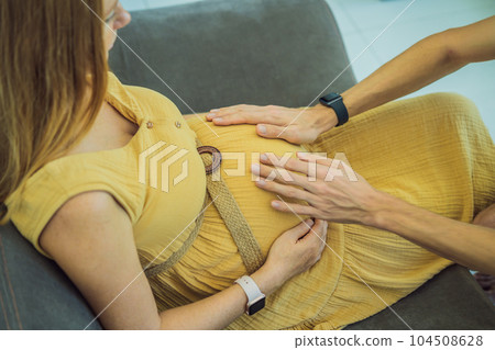 Side view of a future mom and dad holding hands with their heads together. Beautiful beaming couple looking and gazing at the pregnant woman's belly Side view of a future mom and dad holding hands with their heads together. Beautiful beaming couple looking and gazing at the pregnant woman's belly 104508628