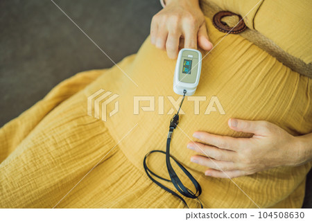 Pregnant woman with pulse oximeter on finger. Doctor measuring oxygen saturation level while visiting expectant mother with coronavirus disease at home, cropped. Pregnancy and covid-19 concept Pregnant woman with pulse oximeter on finger. Doctor measuring oxygen saturation level while visiting expectant mother with coronavirus disease at home, cropped. Pregnancy and covid-19 concept 104508630