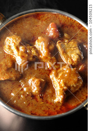 Bird's-eye view of spicy hot Indian curry with chicken on a black background Bird's-eye view of spicy hot Indian curry with chicken on a black background 104509215