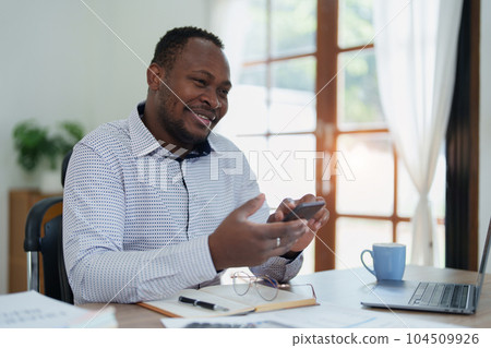 middle aged man American African using smart phone mobile and laptop computer with planning working on financial document, tax, exchange, accounting and Financial advisor. 104509926