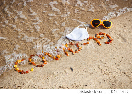 Inscription Covid-19 made of amber stones, protective mask and sunglasses on sand at beach 104511622