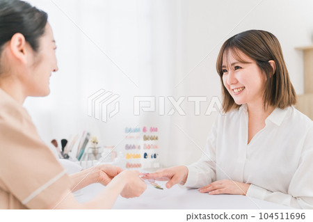 Manicurist and Asian woman counseling color and design using nail tips at nail salon 104511696