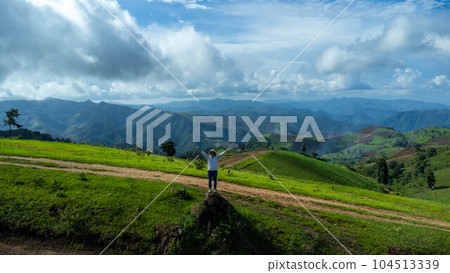 Tourists stand on the rocks enjoying the picturesque hillside views with vast fields on a beautiful sunny day with blue sky and clouds in springtime. 104513339