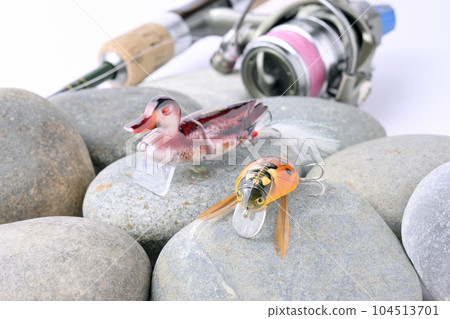 Spinning reel tackle on the background of bird and bug lures on pebbles Spinning reel tackle on the background of bird and bug lures on pebbles 104513701
