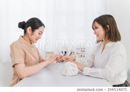 Manicurist sanding at nail salon and Japanese woman receiving treatment Manicurist sanding at nail salon and Japanese woman receiving treatment 104514073