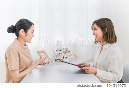 Asian woman holding a tablet with a manicurist showing samples and consulting design options at a nail salon 104514075