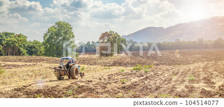 Farmer in tractor working and preparing land in agriculture field with mountain and blue sky 104514077