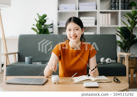 Asian women's hand saving a coin into piggy bank with wooden to calculateon and tablet on the table for business, finance, saving money and property investment concept. Asian women's hand saving a coin into piggy bank with wooden to calculateon and tablet on the table for business, finance, saving money and property investment concept. 104515292