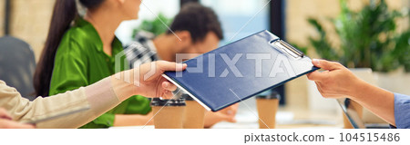 Male coworker giving a folder with documents to his colleague while working in the modern office Male coworker giving a folder with documents to his colleague while working in the modern office 104515486