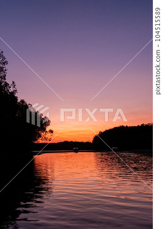 Colorful sky and the sea during the sunrise, with silhouette of the forest on the background 104515589