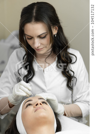 The procedure of deep cleansing of skin of the face is presented, during which a young woman rests and relaxes in beauty salon. The beautician performs cosmetic and medical facial skin care procedure 104517132