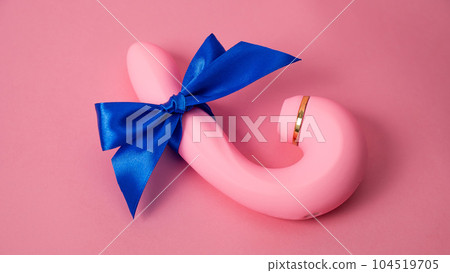 Curved dildo with blue ribbon on pink background.  104519705