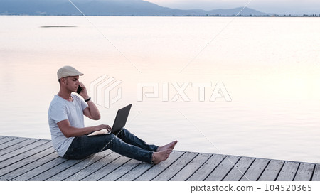 Male freelancer working on pier. Remote worker at sunset Male freelancer working on pier. Remote worker at sunset 104520365