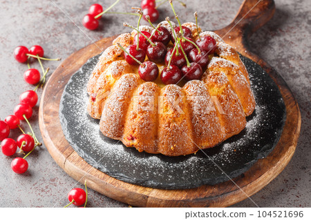 Delicious biscuit vanilla cherry bundt cake decorated with fresh berries and powdered sugar close-up on a wooden board. Horizontal 104521696