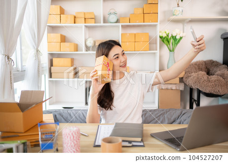 Entrepreneurial Woman Takes Selfies with Products for Online Sales, Working from Home, Identity Verification and Order Confirmation in Online Business, Capturing the Essence of Entrepreneurship. 104527207