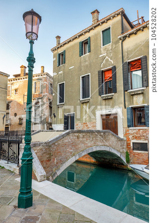 Canal with stone bridge and historic buildings in Venice, Italy. 104528202