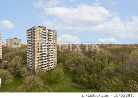 some very tall buildings in the middle of a green area with trees and bushes on either side of the building 104528915