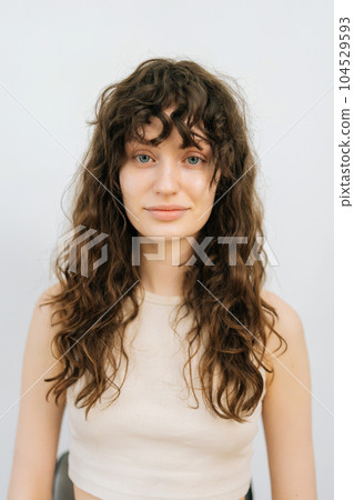 Vertical studio portrait of pretty young woman before applying professional makeup and making stylish hairstyle standing on isolated white background, looking at camera. Concept of fashion and beauty 104529593