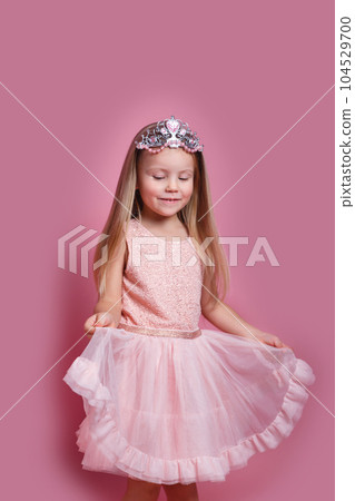 Cute child girl in elegant pink dress and tiara celebrates birthday party on pink background. Cute child girl in elegant pink dress and tiara celebrates birthday party on pink background. 104529700