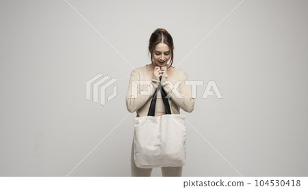 Young happy and excited woman in beige costume with white cotton bag in a hand. Mockup and zero waste concept. 104530418