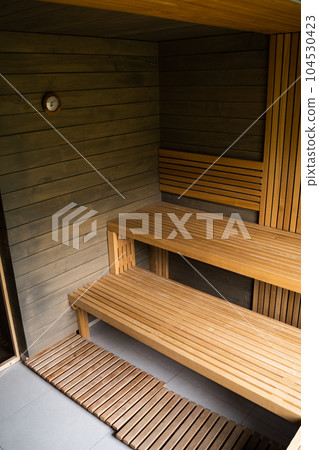 Interior of Finnish sauna, classic wooden sauna with hot steam. Wooden interior baths, wooden benches and loungers, spa complex. 104530423