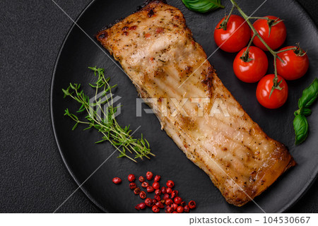 Slice of delicious baked fish with salt, spices and herbs on a ceramic plate 104530667