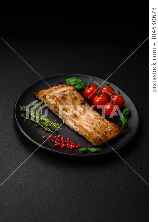 Slice of delicious baked fish with salt, spices and herbs on a ceramic plate 104530673