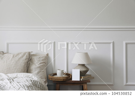 Vintage neutral classic bedroom interior. Cup of coffee on wicker tray, table lamp on wooden bench. Blank greeting card, invitation mockup. White wall background. Gingham bedding set, pillows. 104530852