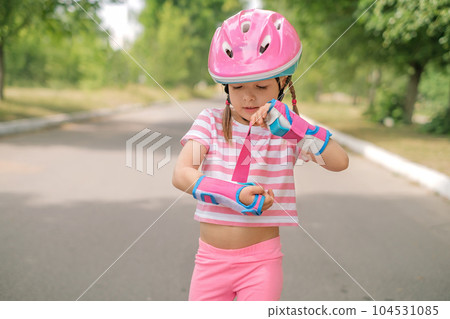 A preschool girl in a sports helmet puts protective gloves on her hands for roller skating training A preschool girl in a sports helmet puts protective gloves on her hands for roller skating training 104531085