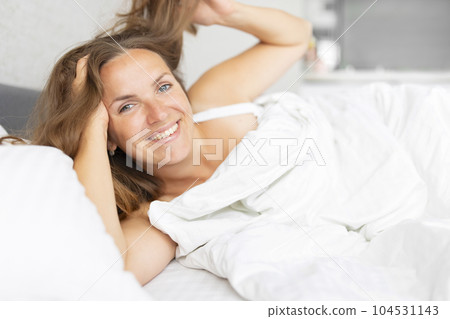 Young smiling attractive brunette woman lies in a big white bed 104531143