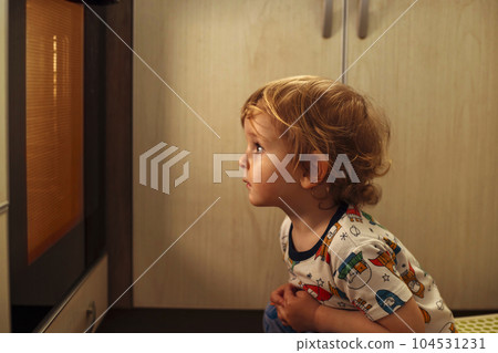 A child is sitting near the oven in the kitchen and waiting. 104531231