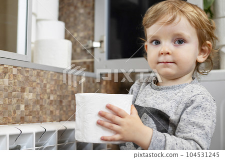 A cute boy is holding toilet paper roll in bathroom. Young boy with toilet paper 104531245