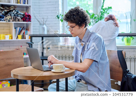 Guy college student typing on laptop, sitting at table in coffee shop with cup of coffee. 104531779