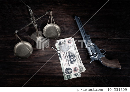 Old west Colt revolver and US banknotes and silver certificates with silver dollar coins and bronze traditional balance scale on wooden table Old west Colt revolver and US banknotes and silver certificates with silver dollar coins and bronze traditional balance scale on wooden table 104531809