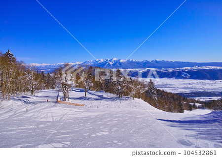 陽光明媚的日子，從富良野滑雪場看到的十勝嶽山脈，以及滑雪者在從富良野地區到北之峰地區的連接路線上滑雪 104532861