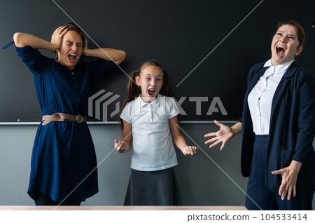 Female teacher, schoolgirl and her mother yell at each other while standing at the blackboard.  104533414