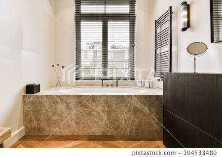 a modern bathroom with wood flooring and marble bathtub in the tub is surrounded by black shuttered windows 104533480