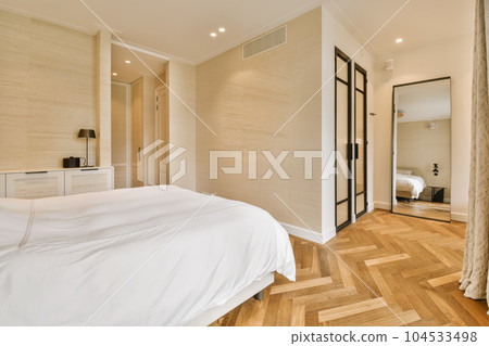 a bedroom with wood flooring and white sheets on the bed, in front of a mirror that is hanging above it 104533498