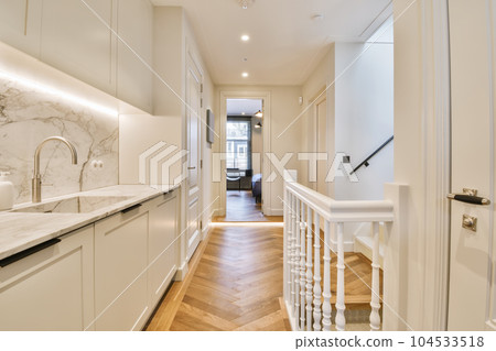 a long narrow hallway with wood flooring and white cabinets on either side by the door to the kitchen area 104533518
