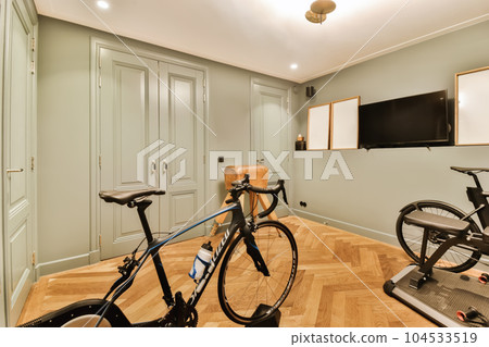 a home gym room with exercise bikes in the corner and tv mounted on the wall above the treading area 104533519