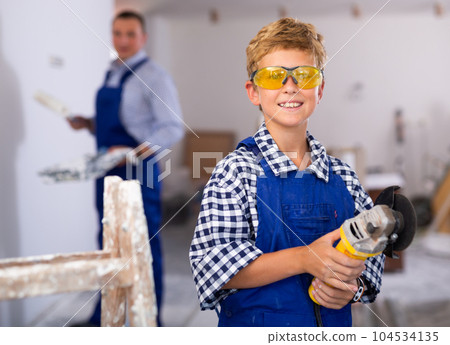 Portrait of little boy in protective glasses with an angle grinder in his hands in room being renovated 104534135