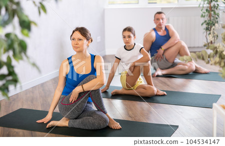Happy middle-aged woman practicing lord of the fishes pose of yoga with her family Happy middle-aged woman practicing lord of the fishes pose of yoga with her family 104534147